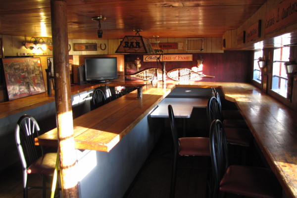 Inside The Dudley Chateau: wooden booths, long bar rail, and neon signs along the downstairs dining room.
